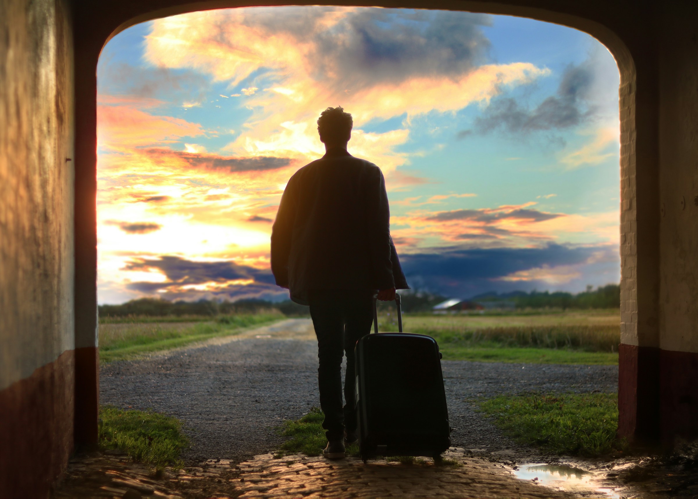 Person with suitcase looking at sunset through an archway