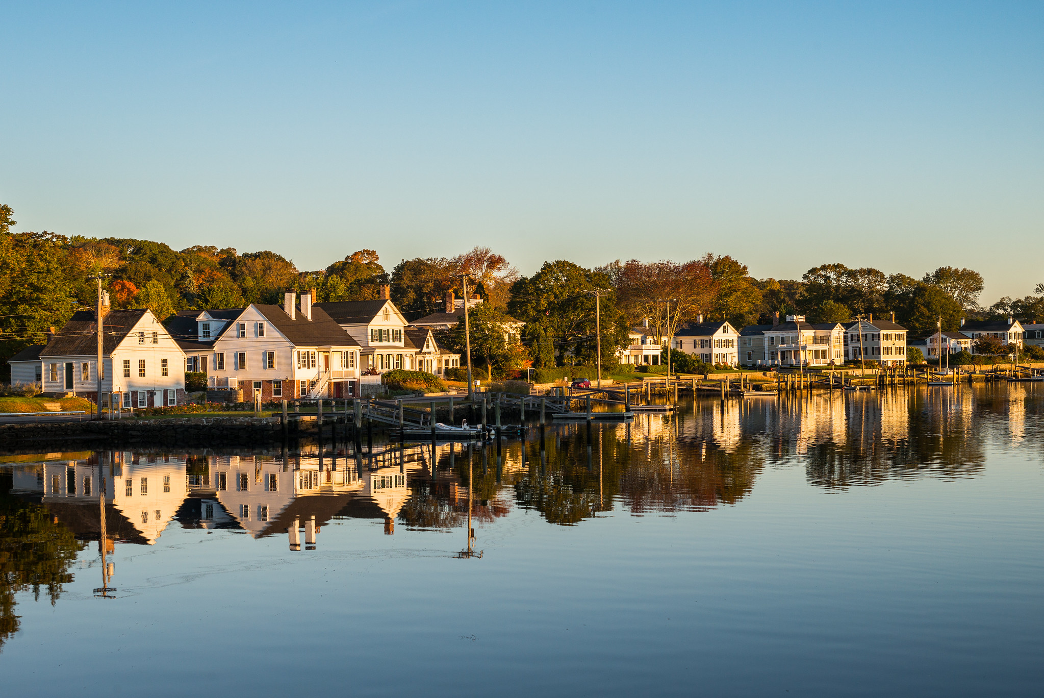 Sunset view of white colonial houses along the Mystic River with perfect reflections in the calm water